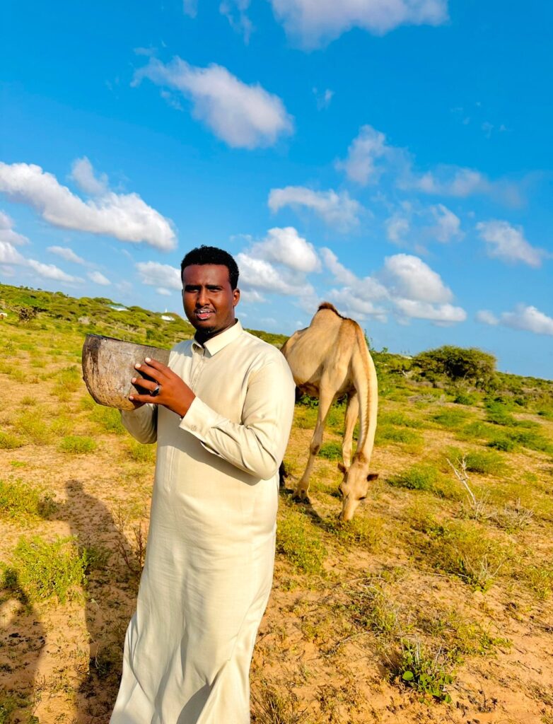 A farmer enjoying fresh, frothy camel milk directly from a traditional bowl after milking, illustrating the consumption of pure milk in camel farming in Kenya.